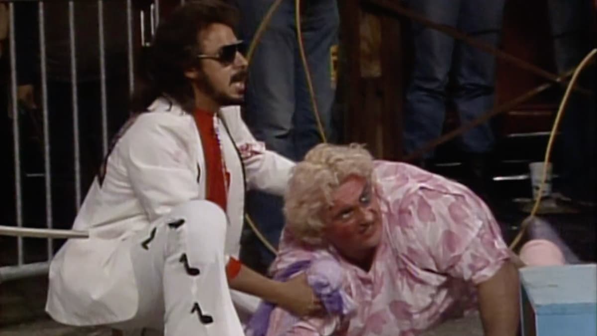Adrian Adonis looking angry as Jimmy Hart consoles him 