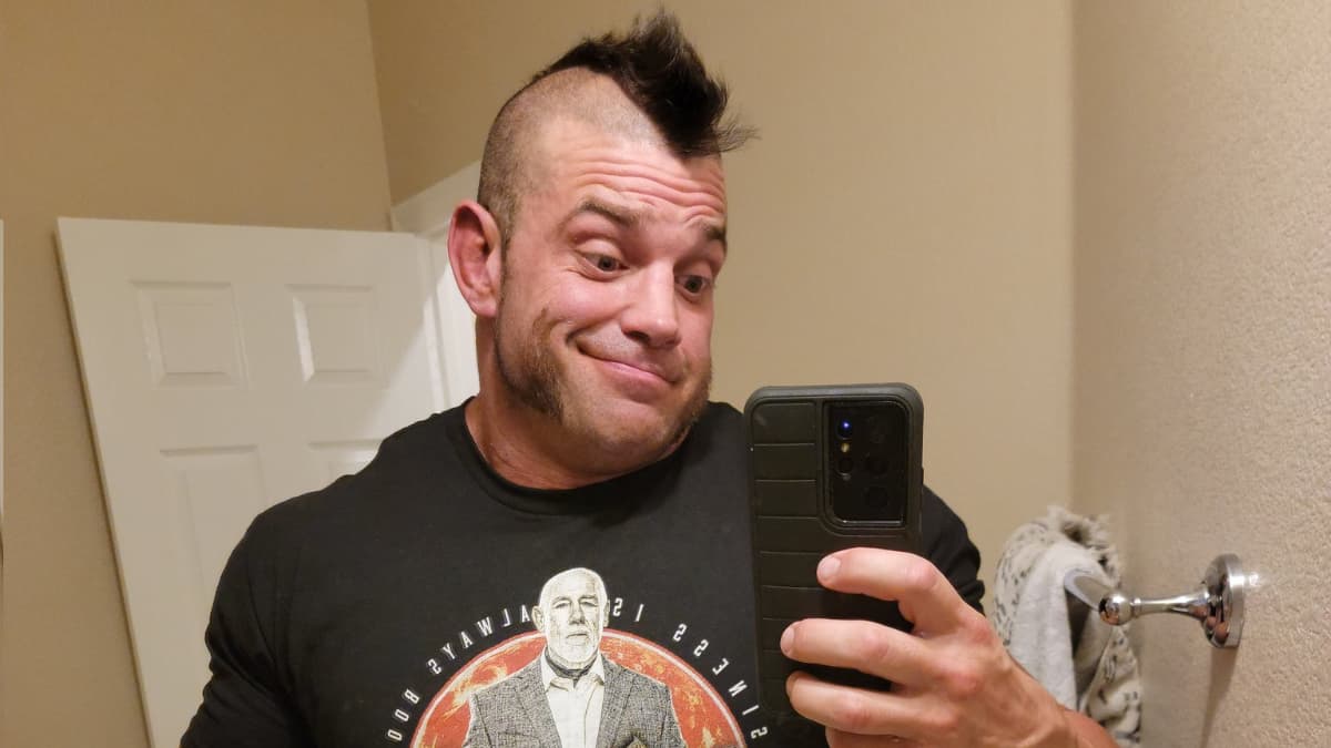 Brian Cage shrugging his shoulders while wearing a Tully Blanchard Enterprises t-shirt