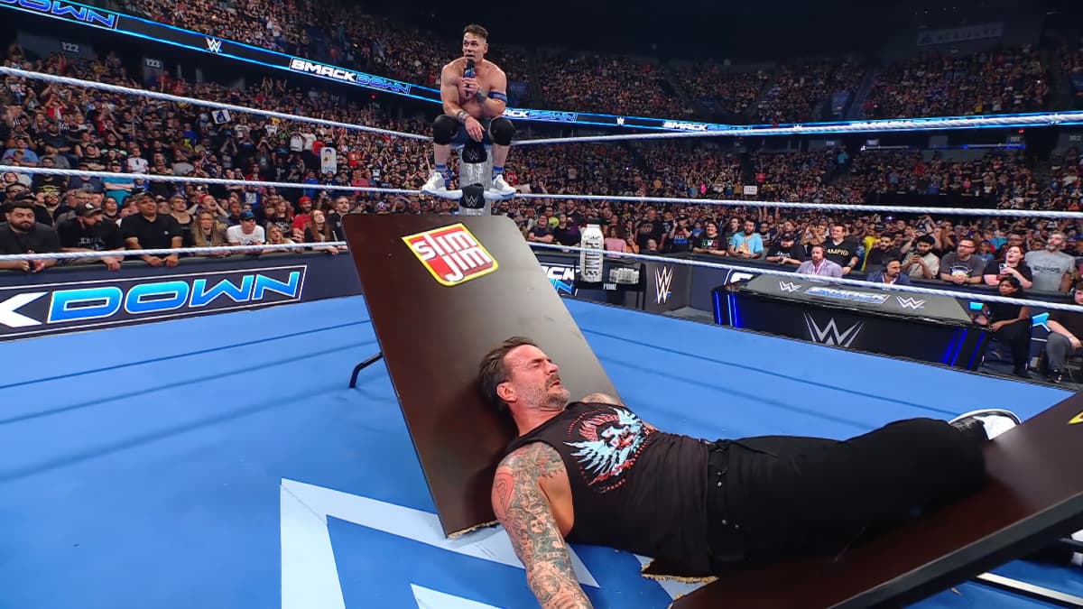 CM Punk lying down in the middle of the ring on a Slim Jim table as John Cena sits on the turnbuckle cutting a promo