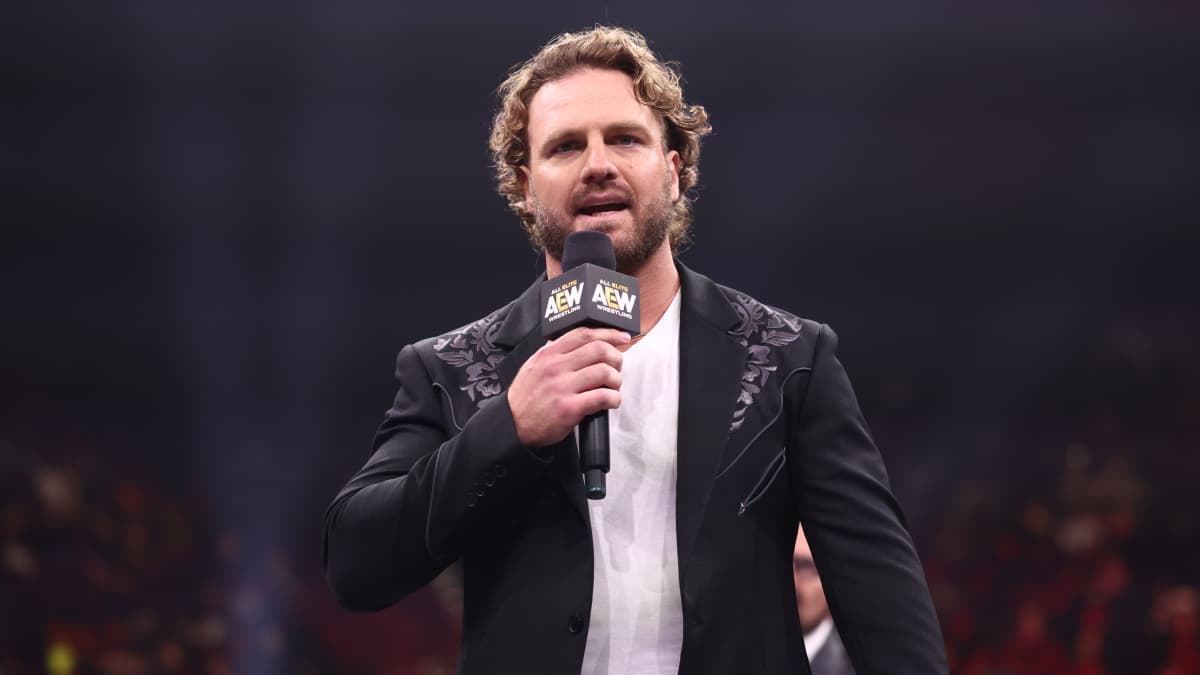Hangman Page wearing a black jacket and holding a microphone