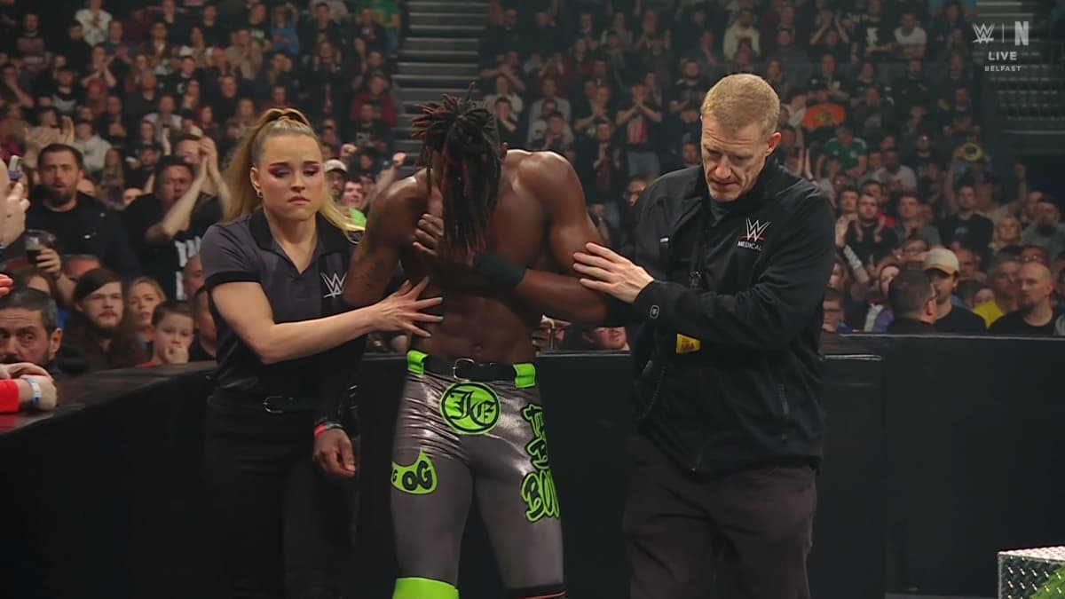 Je'Von Evans with his head down being escorted to the back by WWE referee Jessika Carr on the left and a WWE doctor on the right 