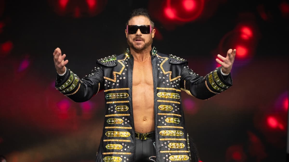 Johnny TV wearing sunglasses and a black and gold trench jacket