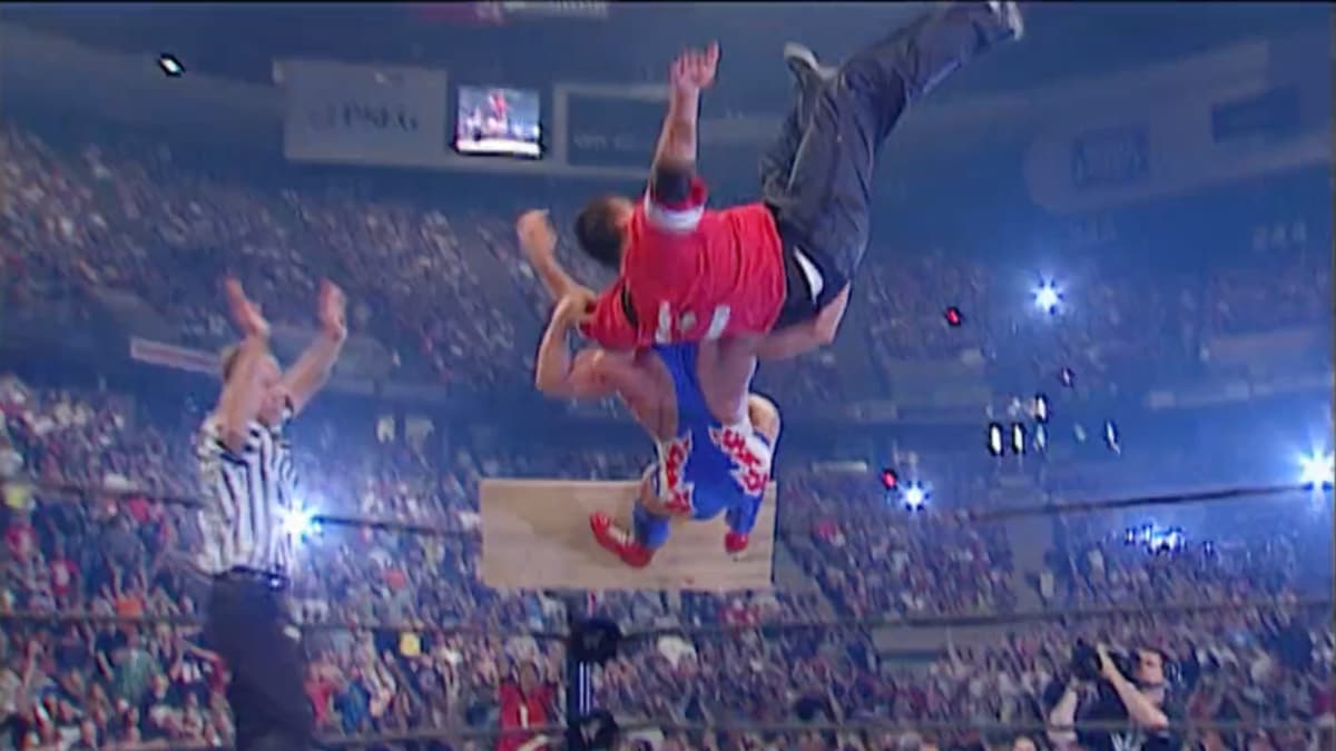 Shane McMahon and Kurt Angle in mid-air as a wooden board tumbles from the top rope during an Avalanche Angle Slam