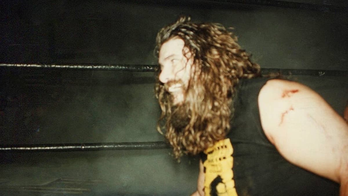 Mick Foley smiling while smoke rises behind him