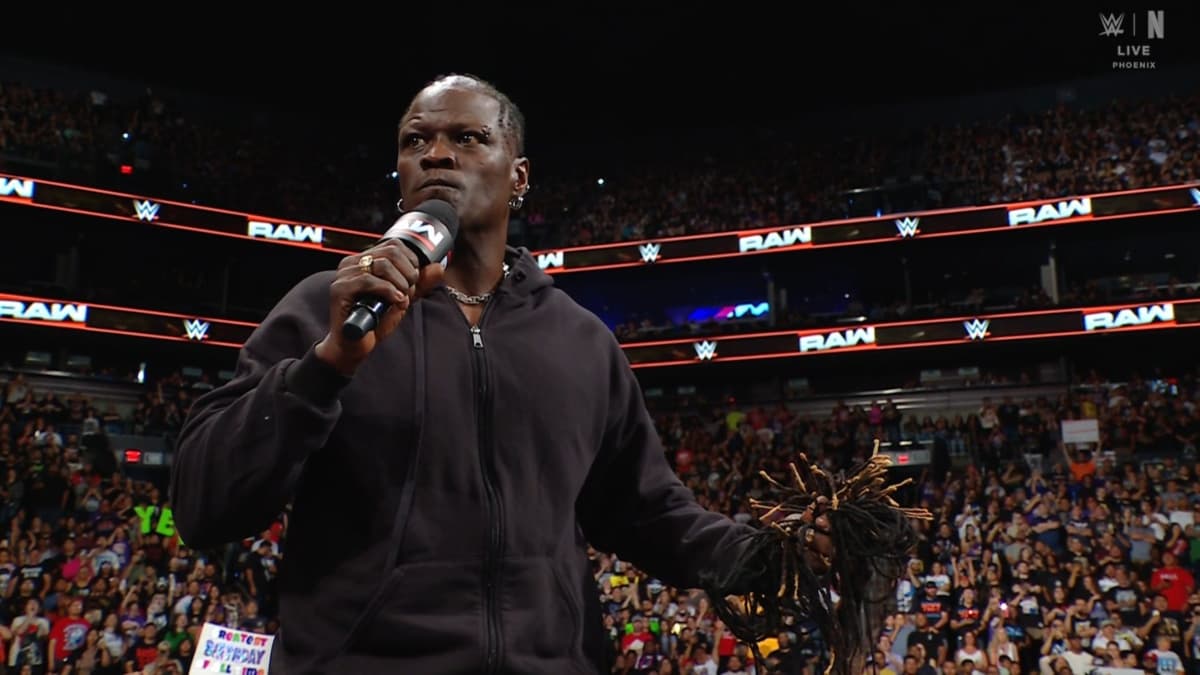 WWE star Ron Killings holds his hair in his left hand and a microphone in his right after cutting his hair off with scissors on WWE Raw