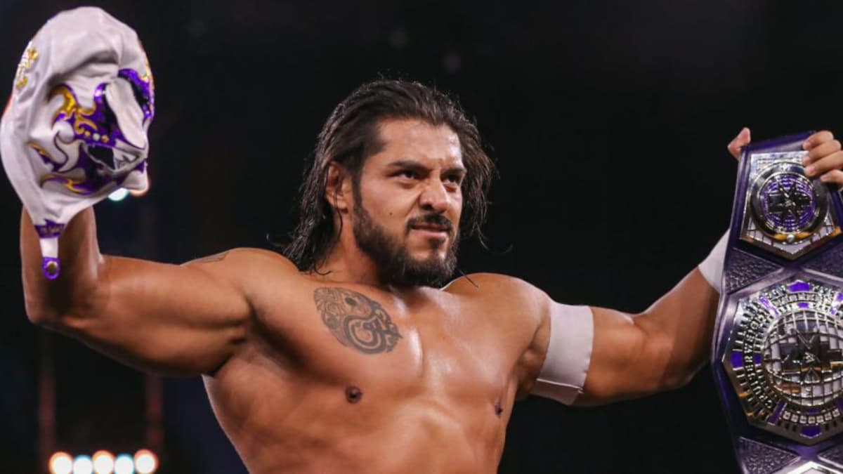 Santos Escobar holds up a lucha mask in one hand and the WWE Cruiserweight Championship in the other