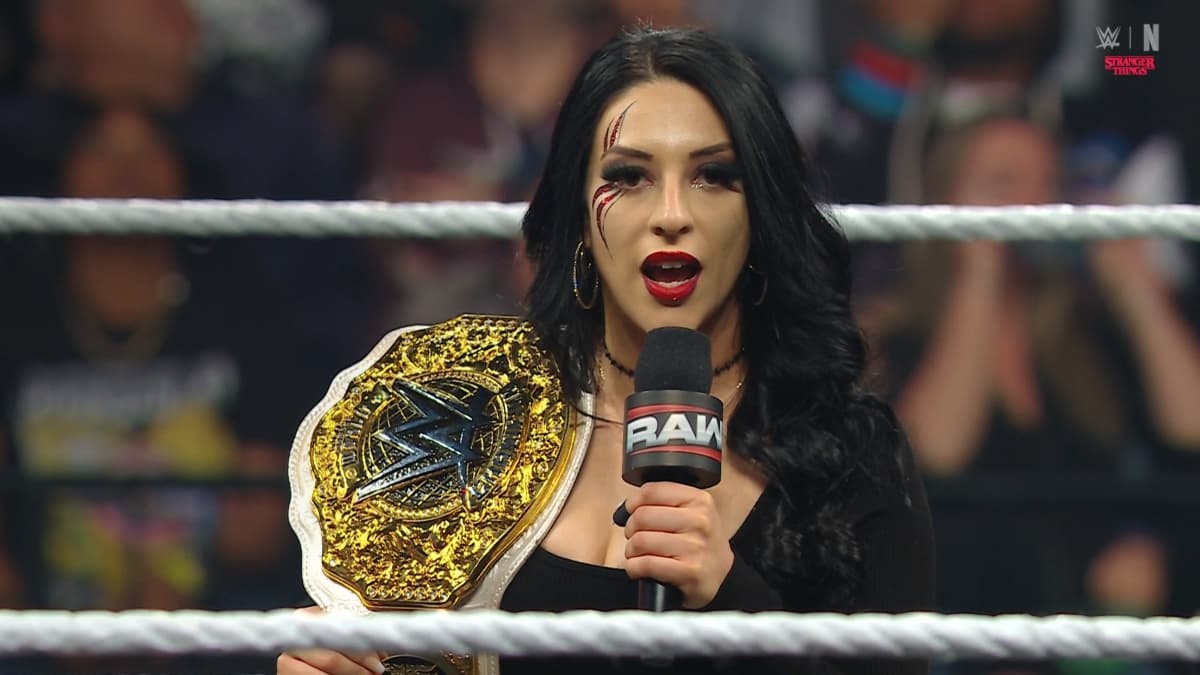 Stephanie Vaquer holding a WWE Raw microphone with the WWE Women's World Title over her right shoulder
