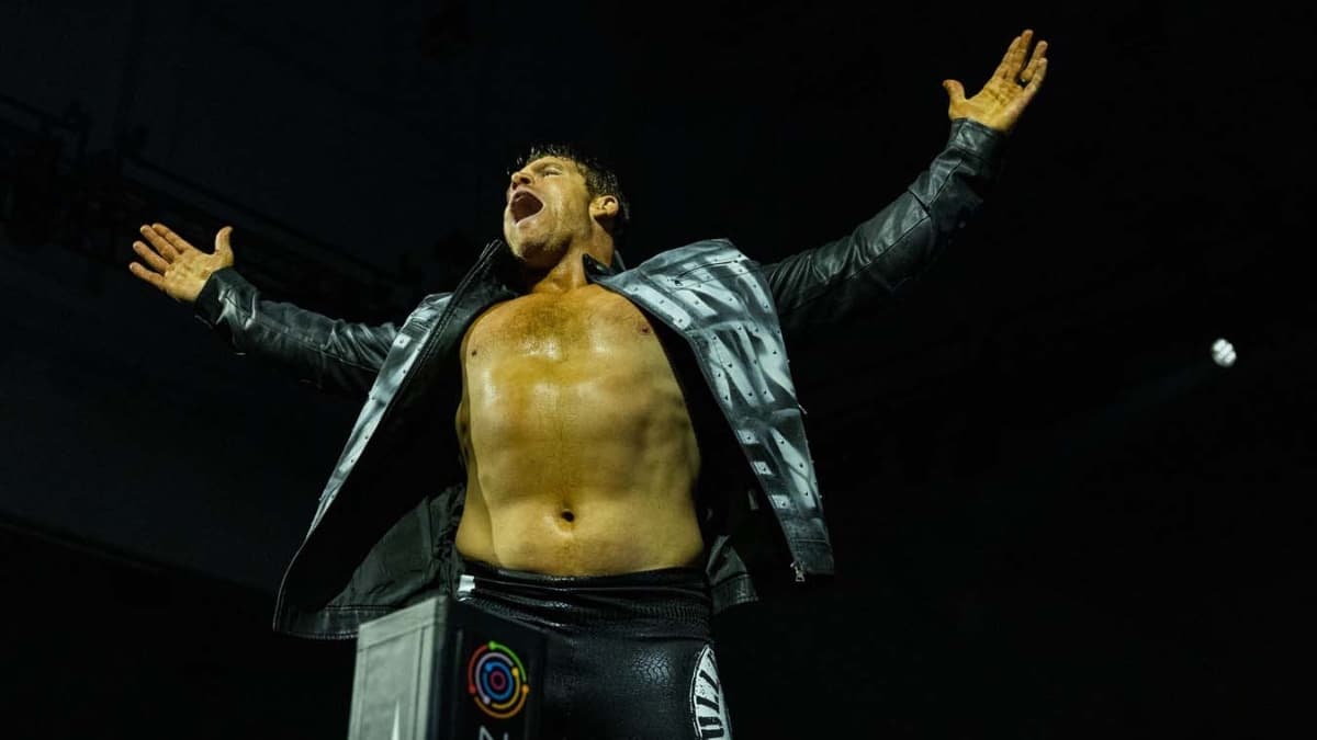 Steve Maclin in a black jacket with his arms outstretched on the ring apron