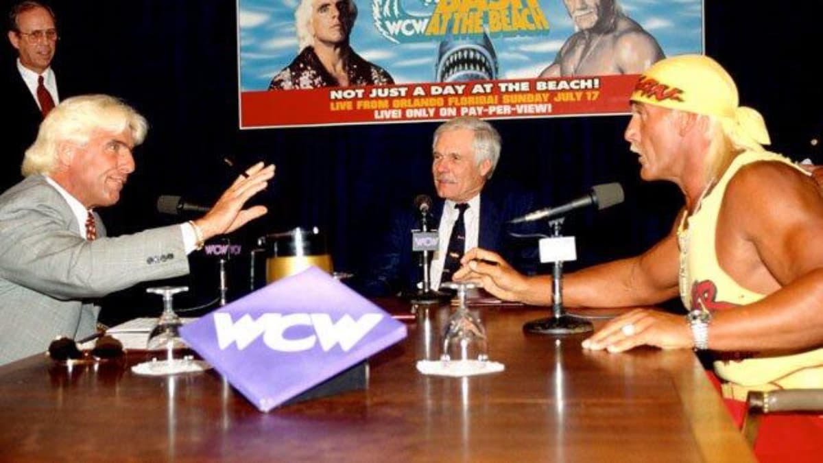 Ted Turner sitting between Ric Flair and Hulk Hogan, who are arguing at a table