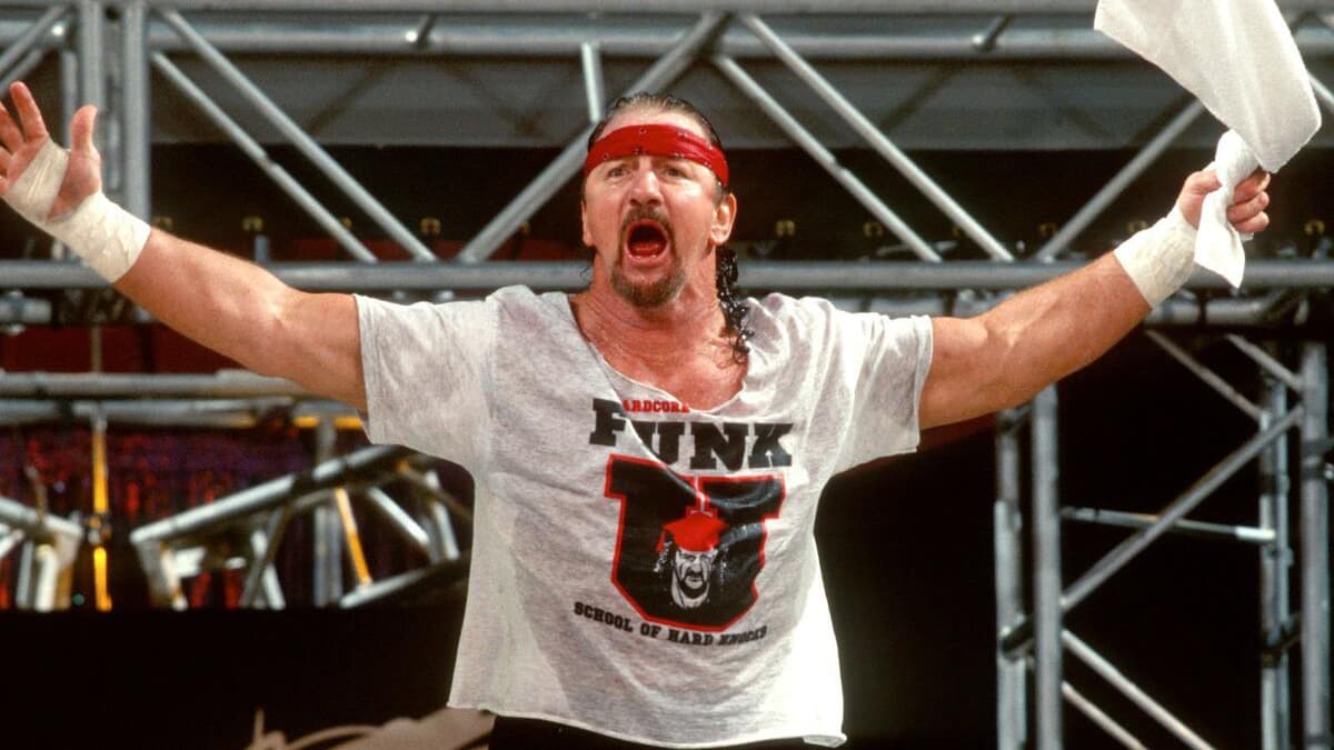Terry Funk making his way to the ring with his arms outstretching, holding a white towel and wearing a red headband and white, wet t-shirt