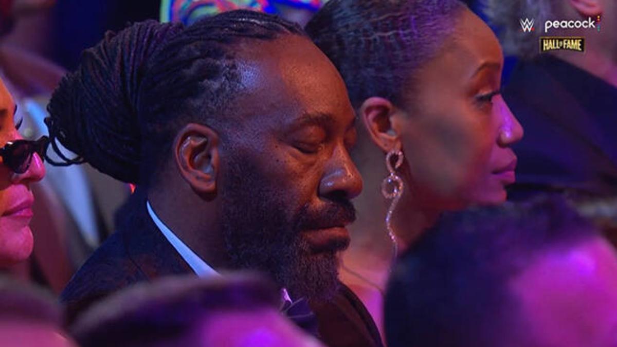A suited Booker T sits with his eyes closed in a crowd
