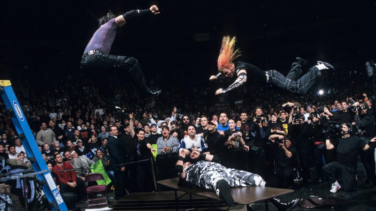 Matt and Jeff Hardy in mid air diving onto Bubba Ray Dudley on a table in front of a crowd