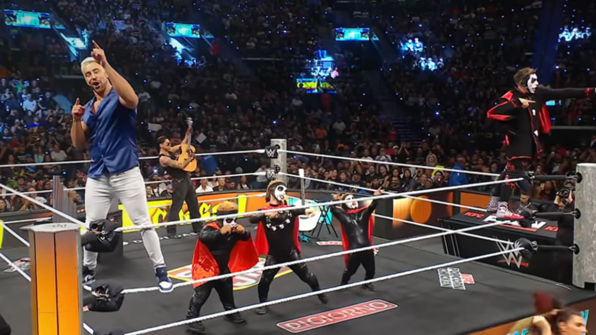 Joe Hendry and Danhausen dancing on the top rope with three dwarfs and Ryan Garcia standing behind them playing the guitar