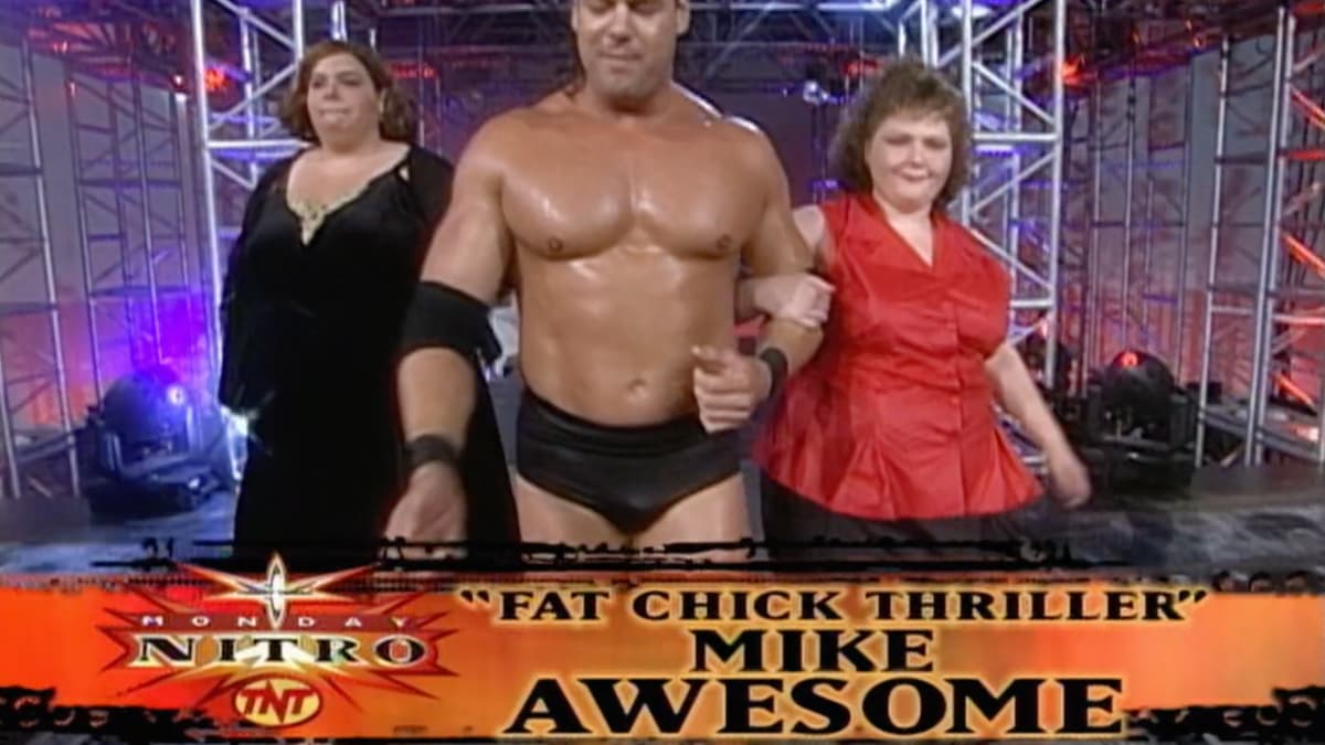 Mike Awesome walking to the ring with two obese women as 'Fat Chick Thriller Mike Awesome' is displayed on the roll call