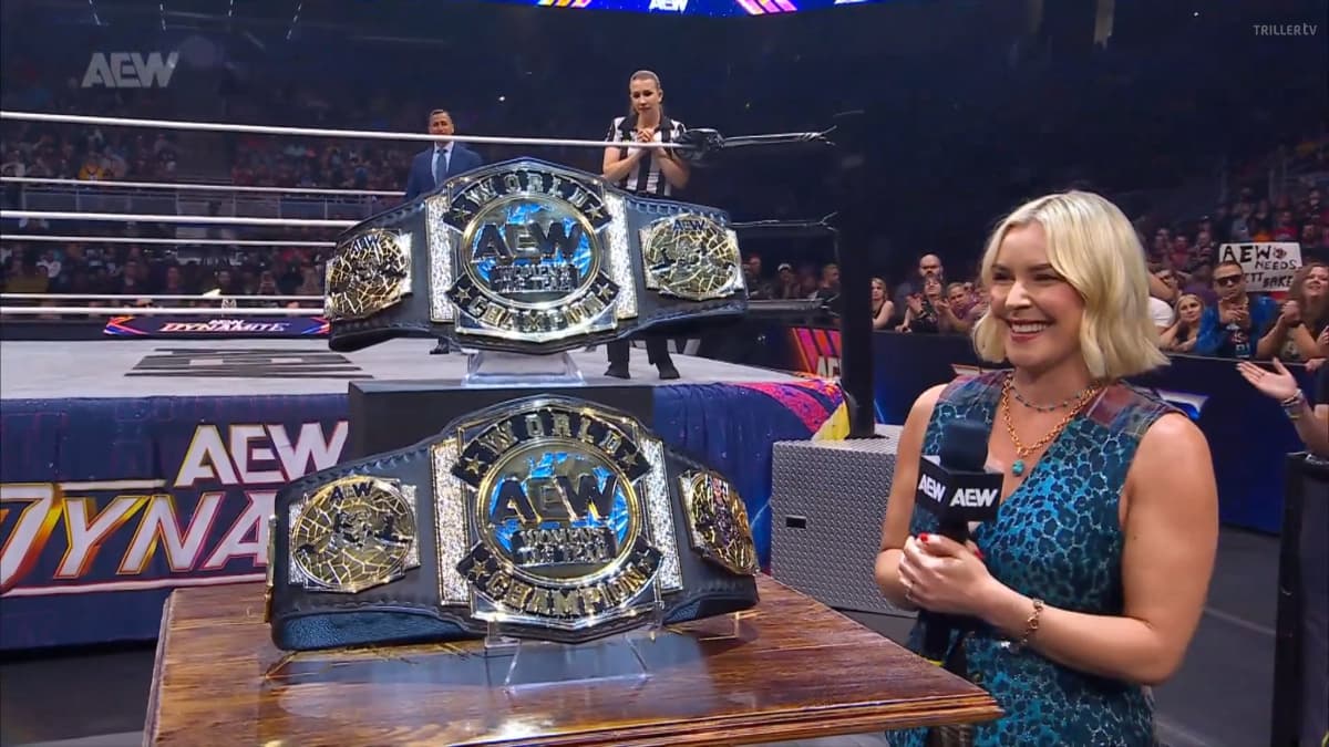 Renee Paquette looks at a set of AEW championship belts in front of a wrestling ring