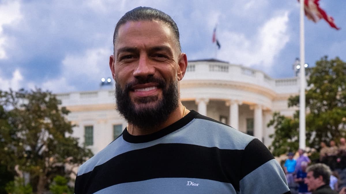 Roman Reigns in a blue and black striped Dior t-shirt smiling in front of the White House