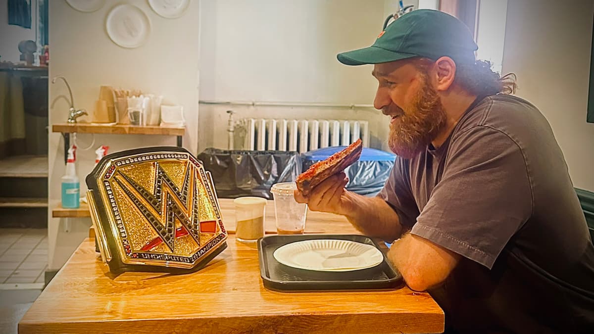 Sami Zayn eating pizza while looking at the WWE Championship
