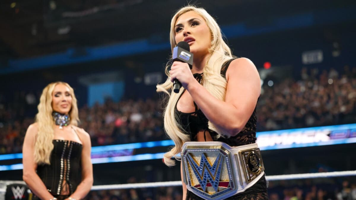 Tiffany Stratton speaking into the mic as Charlotte Flair stands in the ring