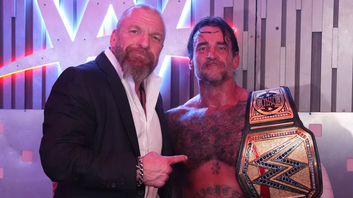 Triple H pointing at CM Punk, who has the WWE Championship over his shoulder