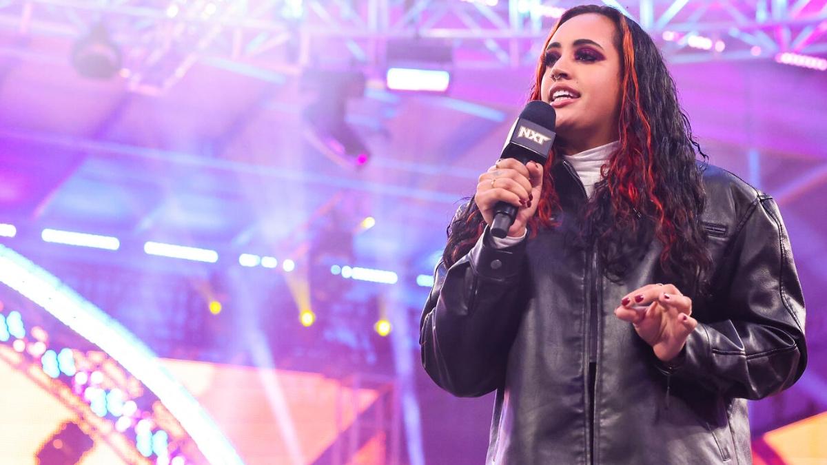 Ava holding a microphone and wearing a jacket on WWE NXT