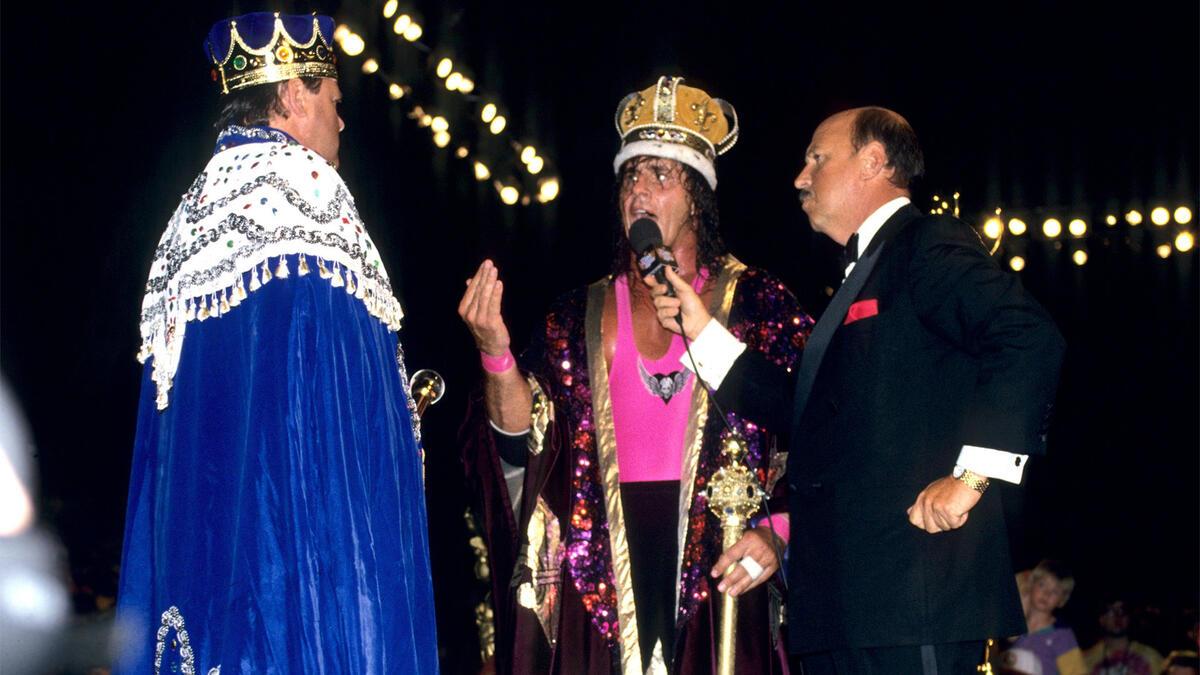Bret Hart wearing a cape and crown, talking to Jerry Lawler (also in a cape and crown), while Gene Okerlund holds a microphone