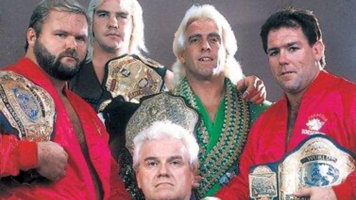 Arn Anderson, Barry Windham, Ric Flair and Tully Blanchard posing with pro wrestling title belts as JJ Dillon kneels below them