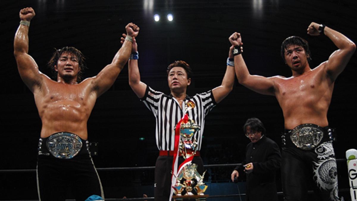 Hiroshi Tanahashi and Shinsuke Nakamura having their arms raised by Red Shoes Uno