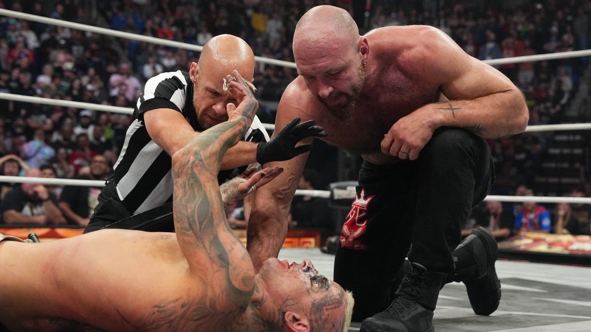 Jon Moxley looking down at Darby Allin as Bryce Remsburg puts his hands between them