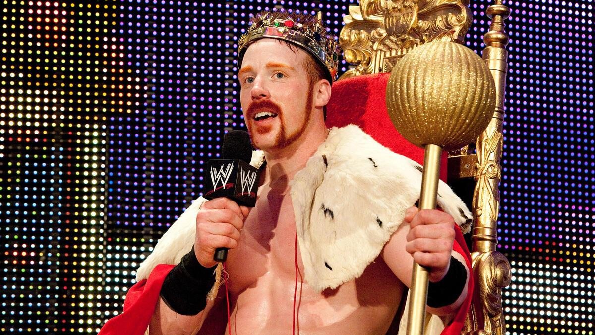 Sheamus sitting in a throne wearing a cape and crown, holding a sceptre