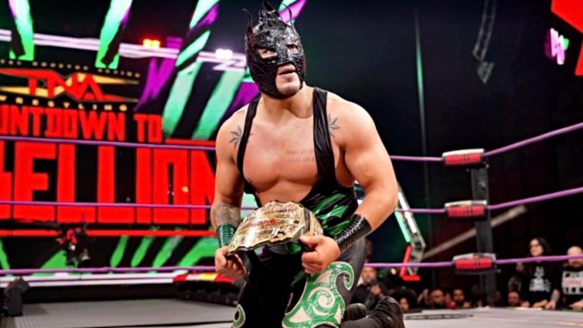 Laredo Kid on his knees holding a championship title belt in a TNA ring
