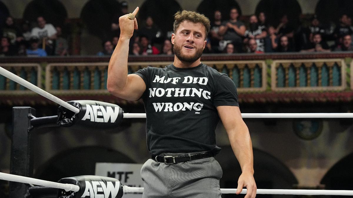 MJF in a t-shirt and suit trousers holds up his pinky finger in an AEW wrestling ring