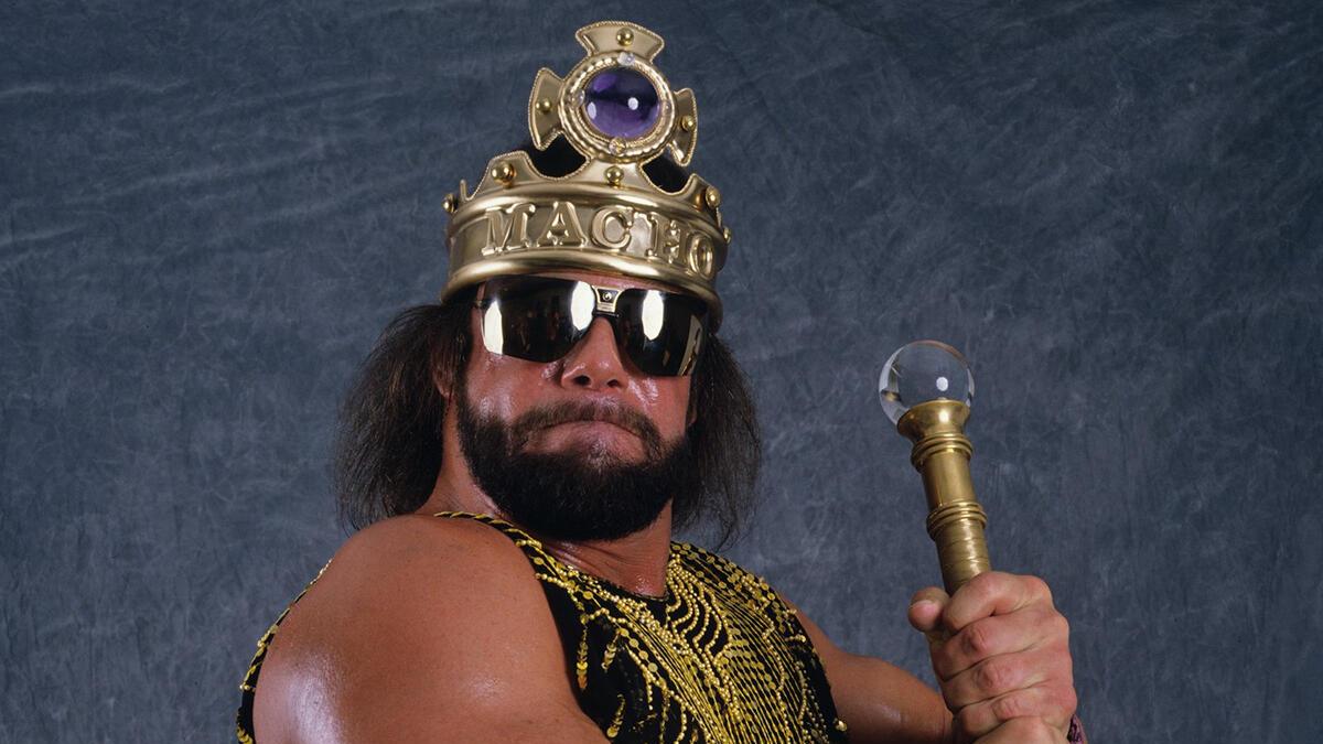 Randy Savage wearing his Macho King crown and holding a sceptre while wearing a purple vest emblazoned with gold