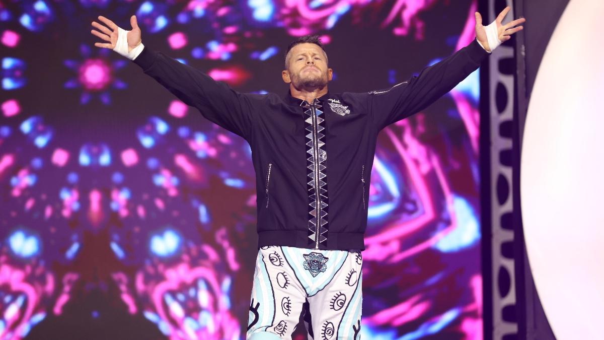Matt Sydal wearing pink and white trousers and a black jacket with his arms outstretched