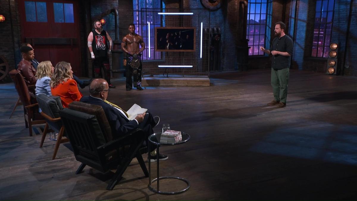 Andrew Bowers speaking to the Dragons on Dragons' Den as Rory Coyle and a topless Man Like Dereiss stand to the side