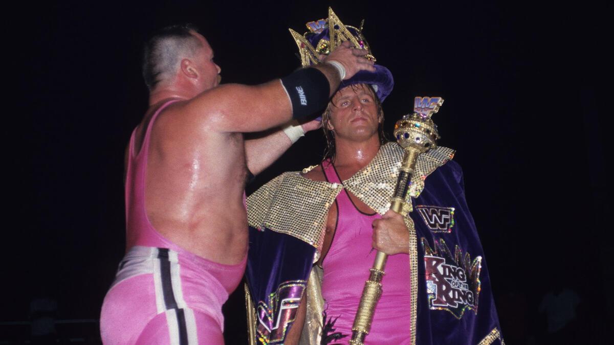 Jim Neidhart placing the crown on Owen Hart's head, who is already wearing a cape and holding a sceptre