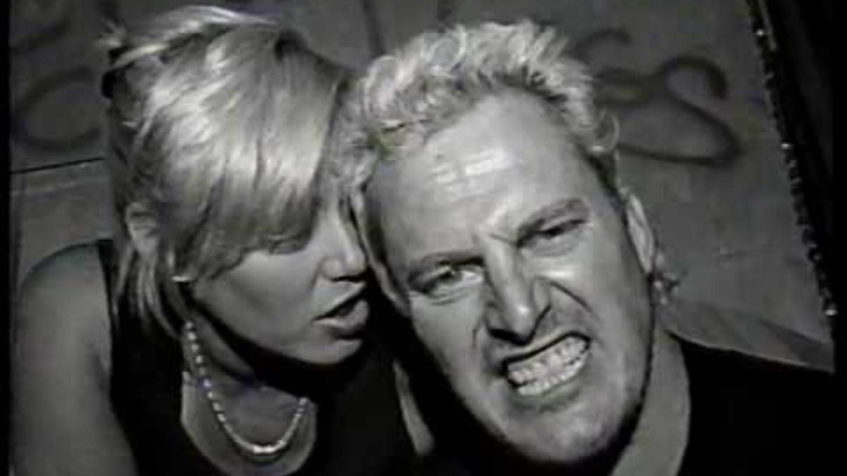 Sandman baring his teeth as Missy Hyatt whispers into his ear