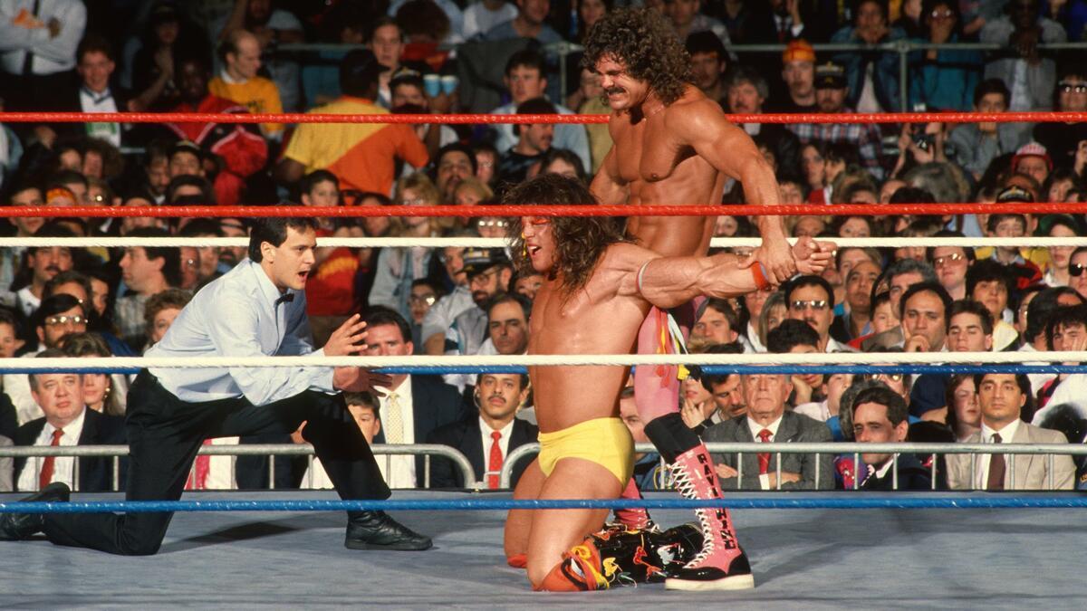 Rick Rude with his knee in Ultimate Warrior's back at WWE WrestleMania V